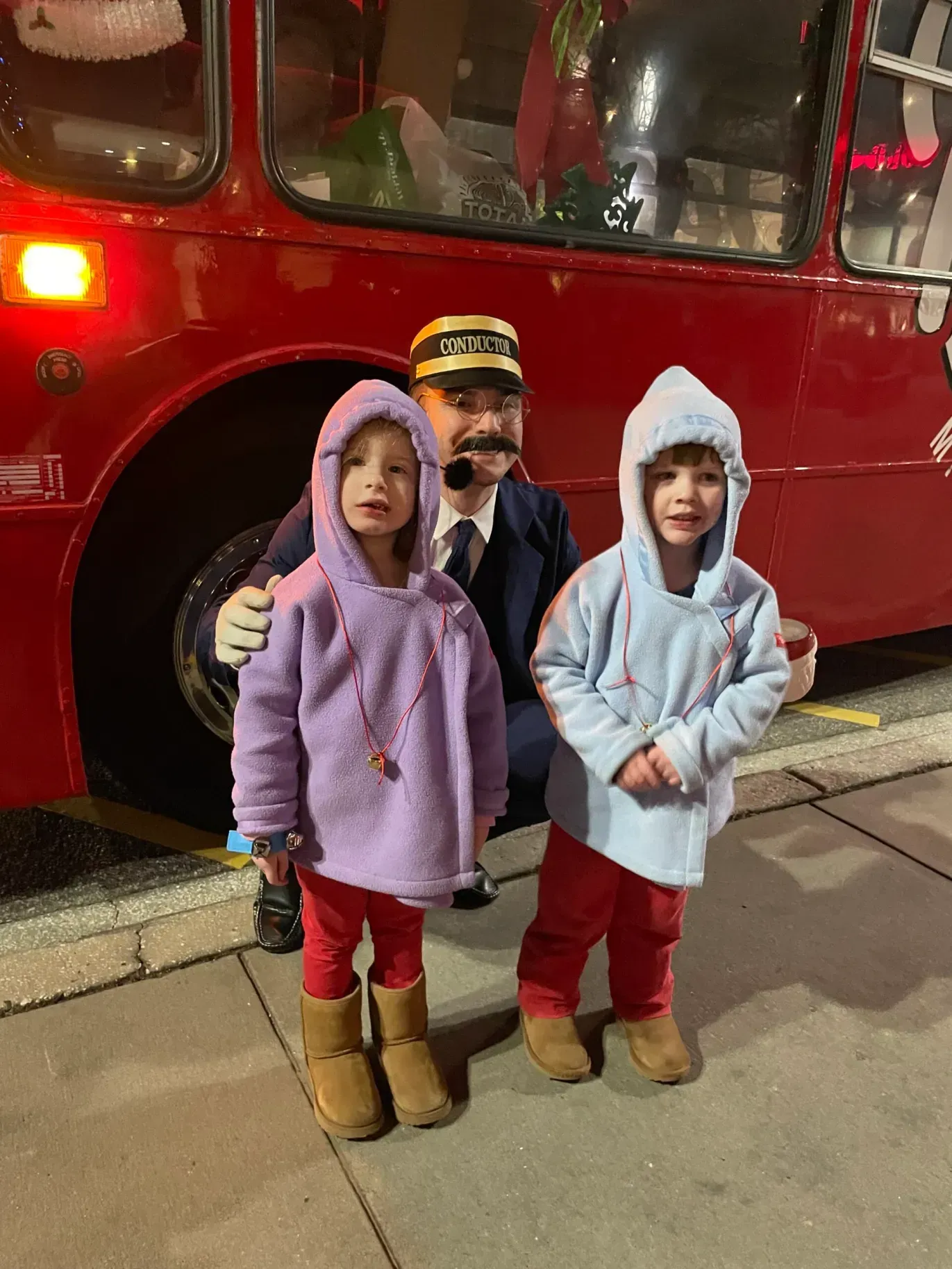 A man and two little girls are standing in front of a red bus.