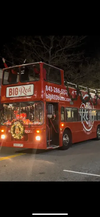 A red double decker bus is driving down a street at night.
