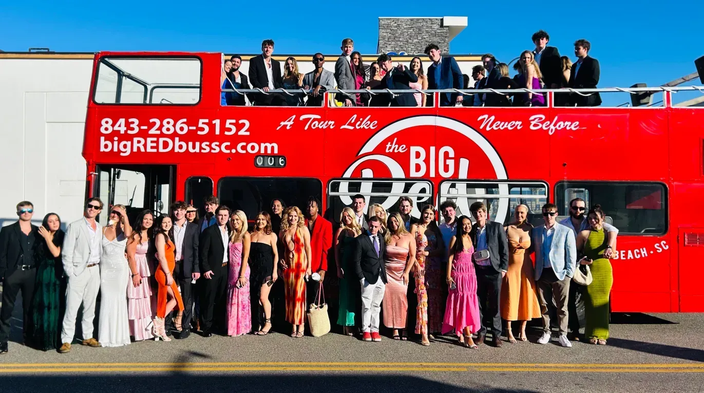 A large group of people are standing in front of a red double decker bus.
