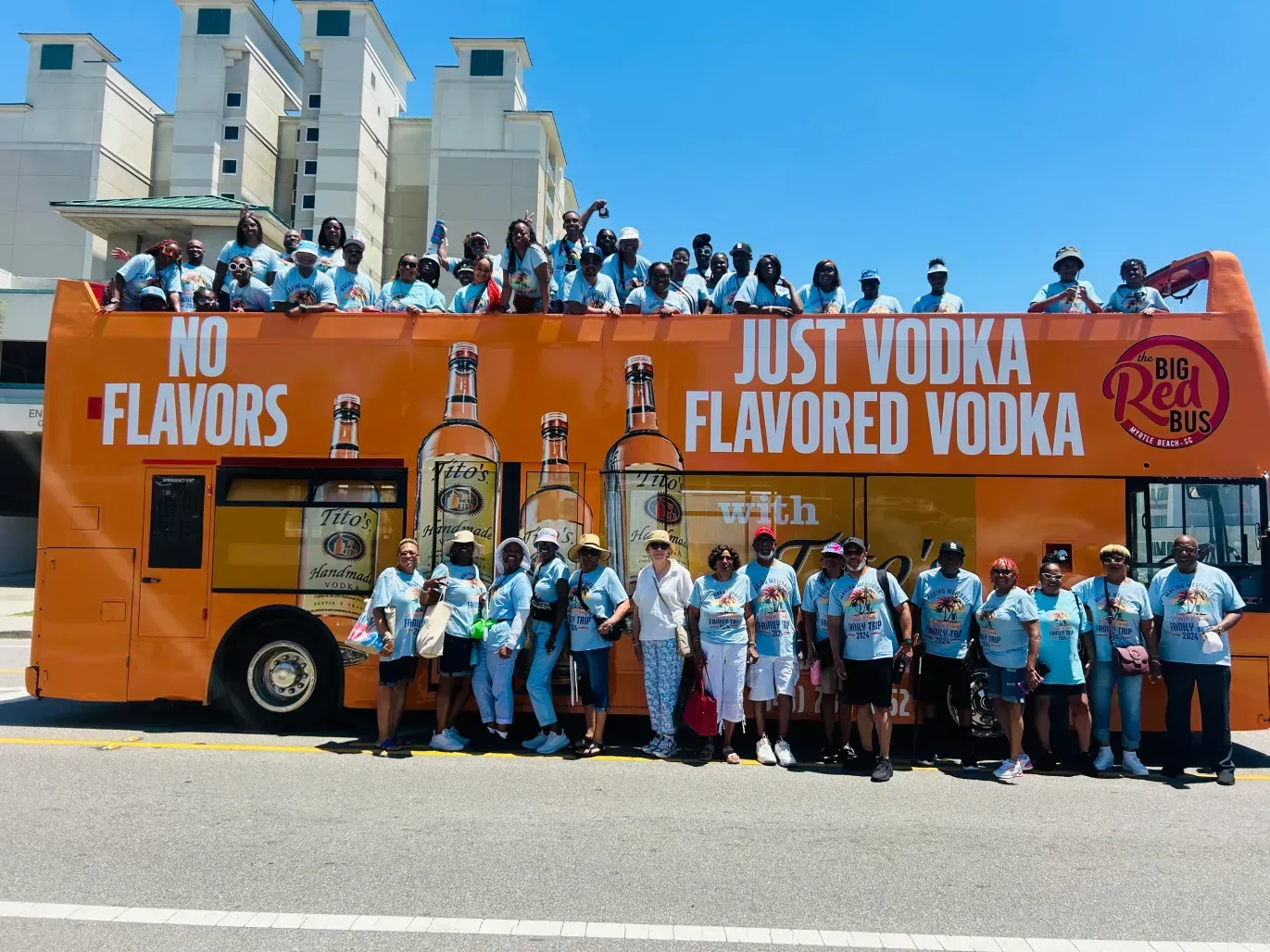 A group of people standing in front of a bus that says just vodka flavored vodka