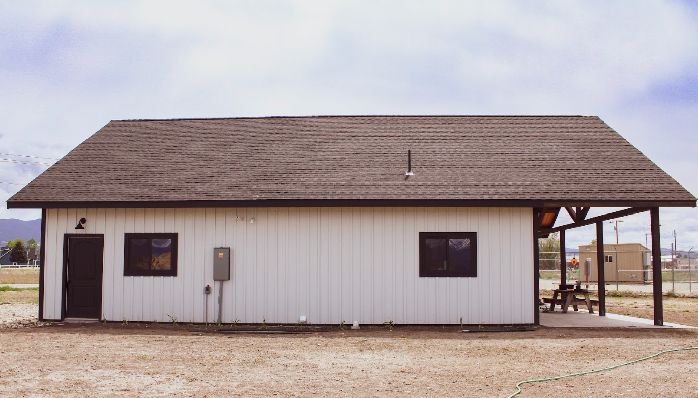 A white metal building is sitting in the middle of a dirt field.