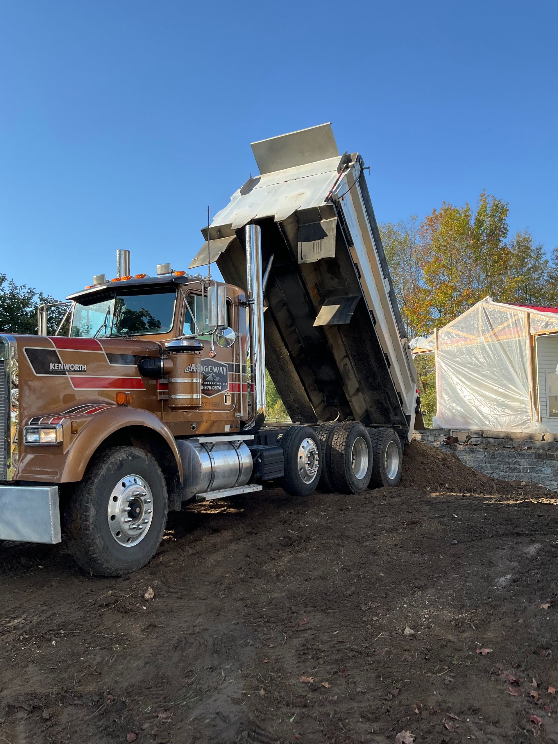 Dump truck unloading dark soil at a worksite under a blue sky