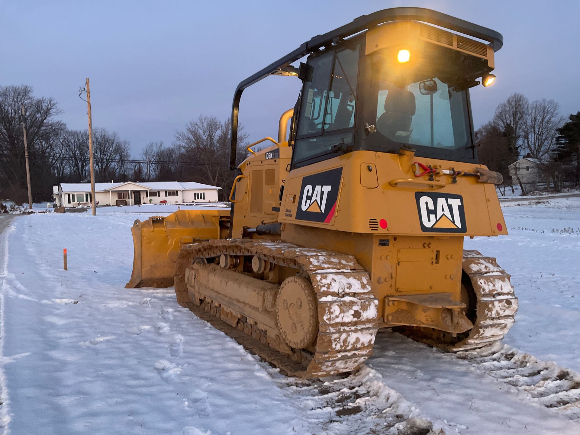 Yellow CAT bulldozer clearing snow on a snowy road at dusk