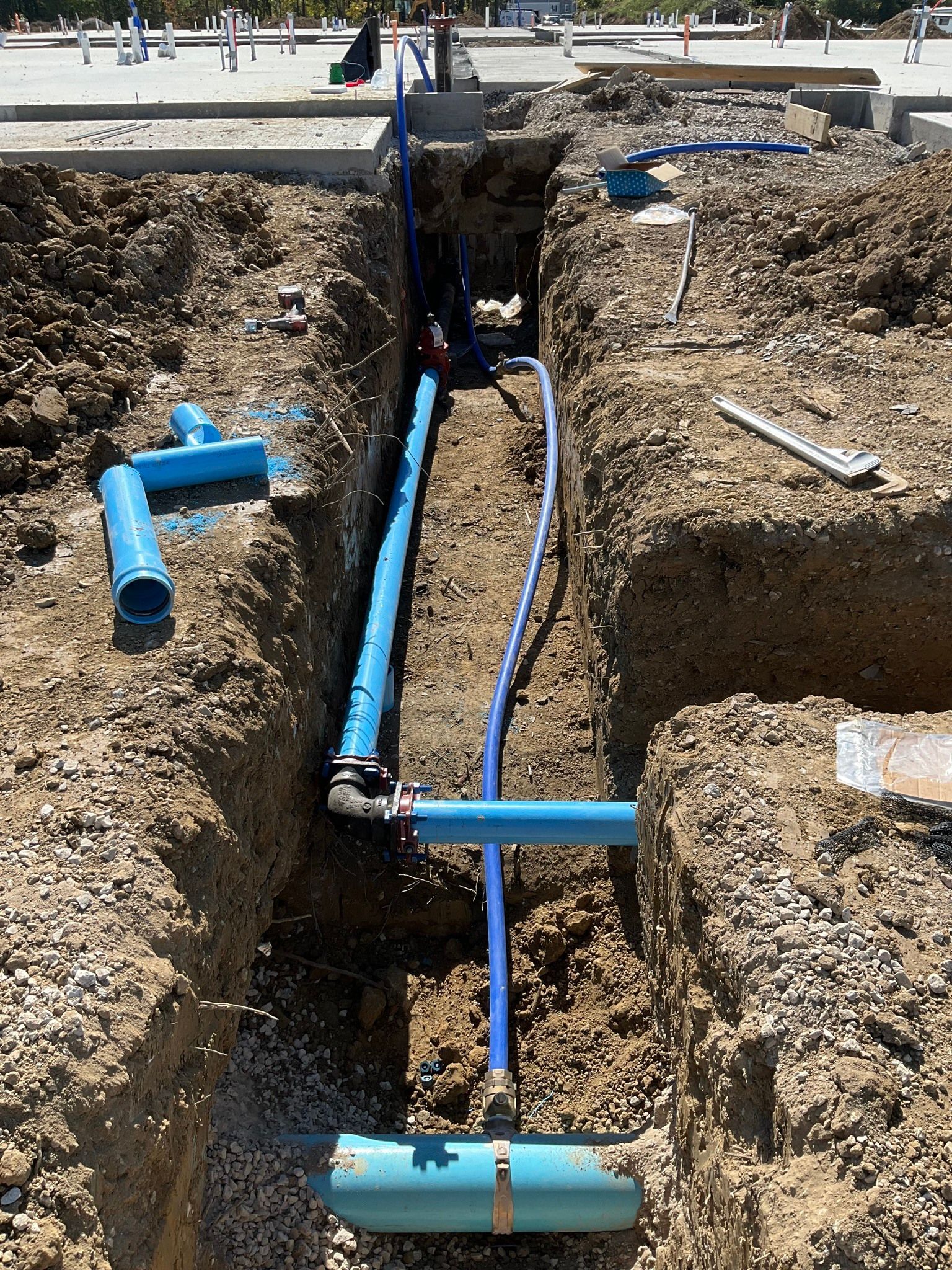 Blue utility pipes laid in a trench at a construction site, with soil walls and exposed fittings.