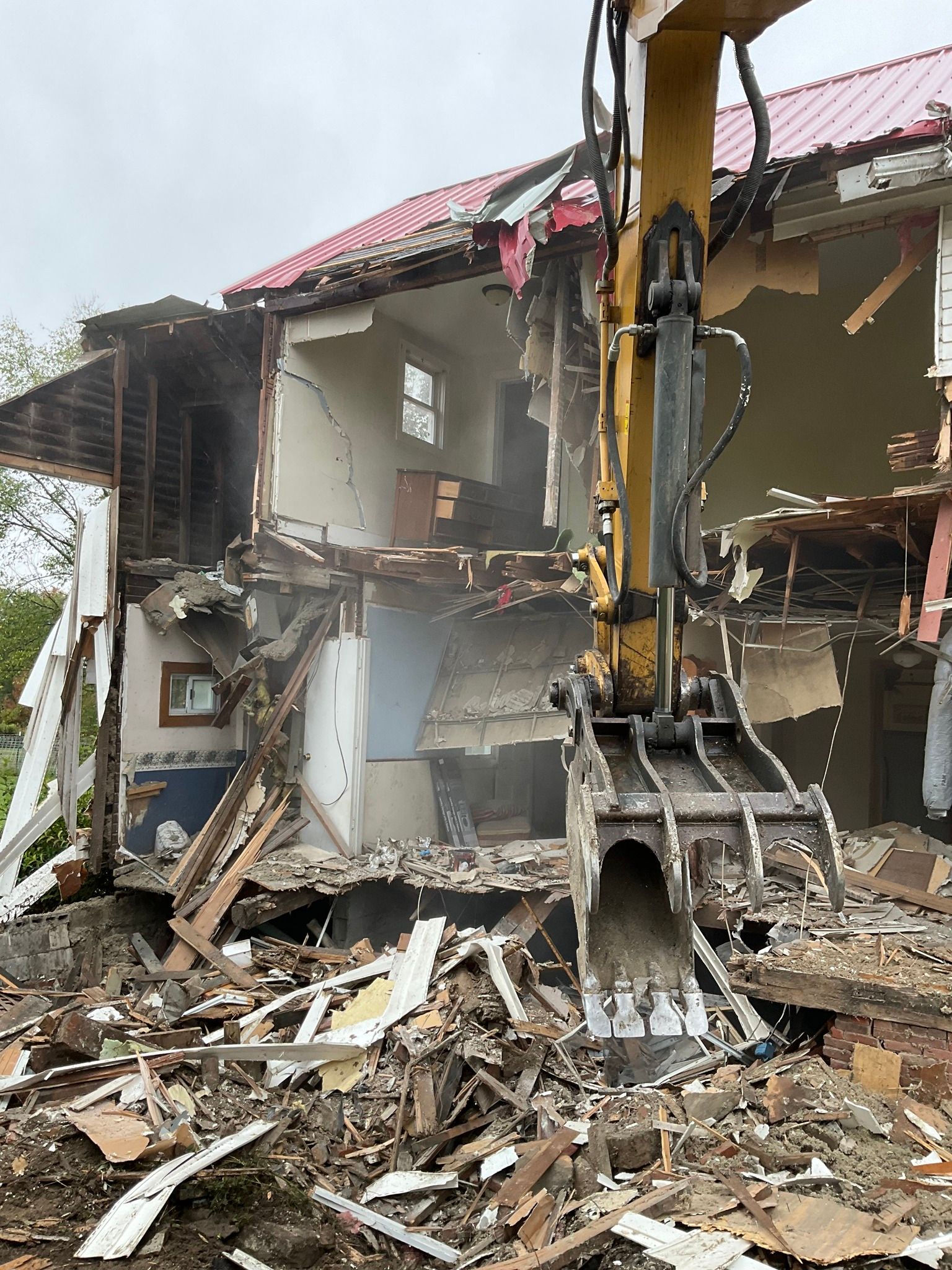 Excavator demolishing a damaged building amid rubble and debris.