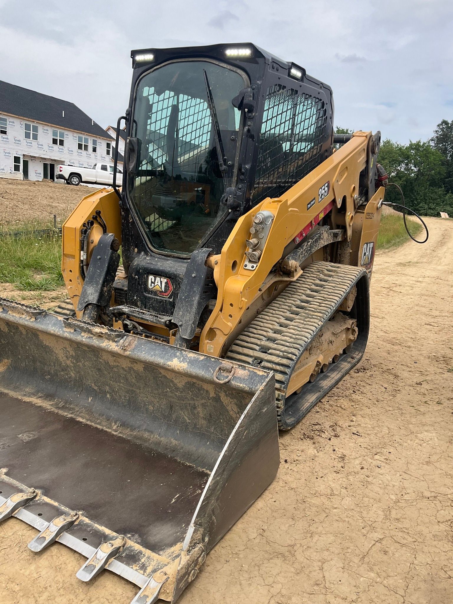 Yellow skid steer loader with bucket on a dirt lot near buildings and grass
