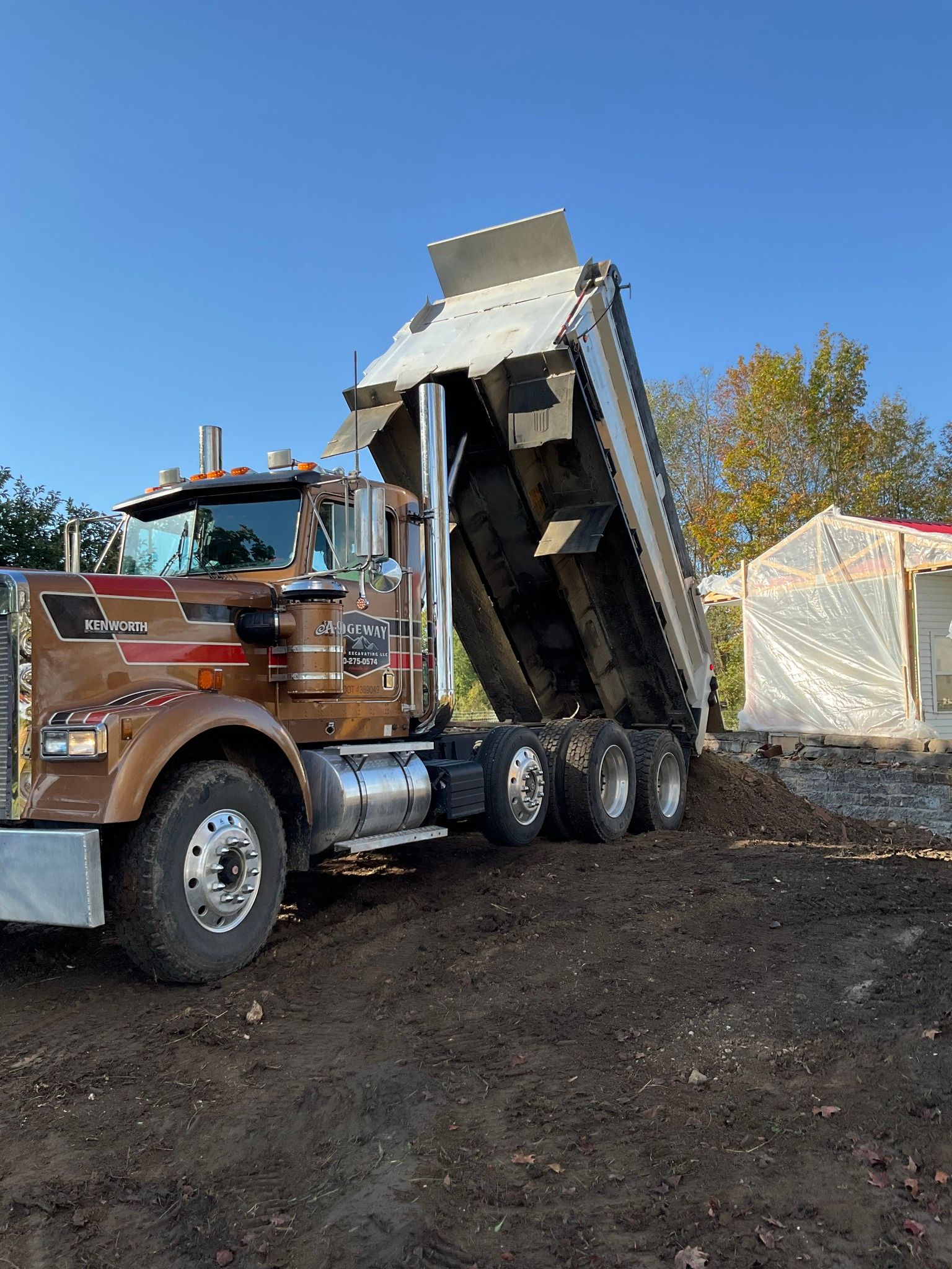 Dump truck tipping a load of dark gravel at a construction site under a blue sky