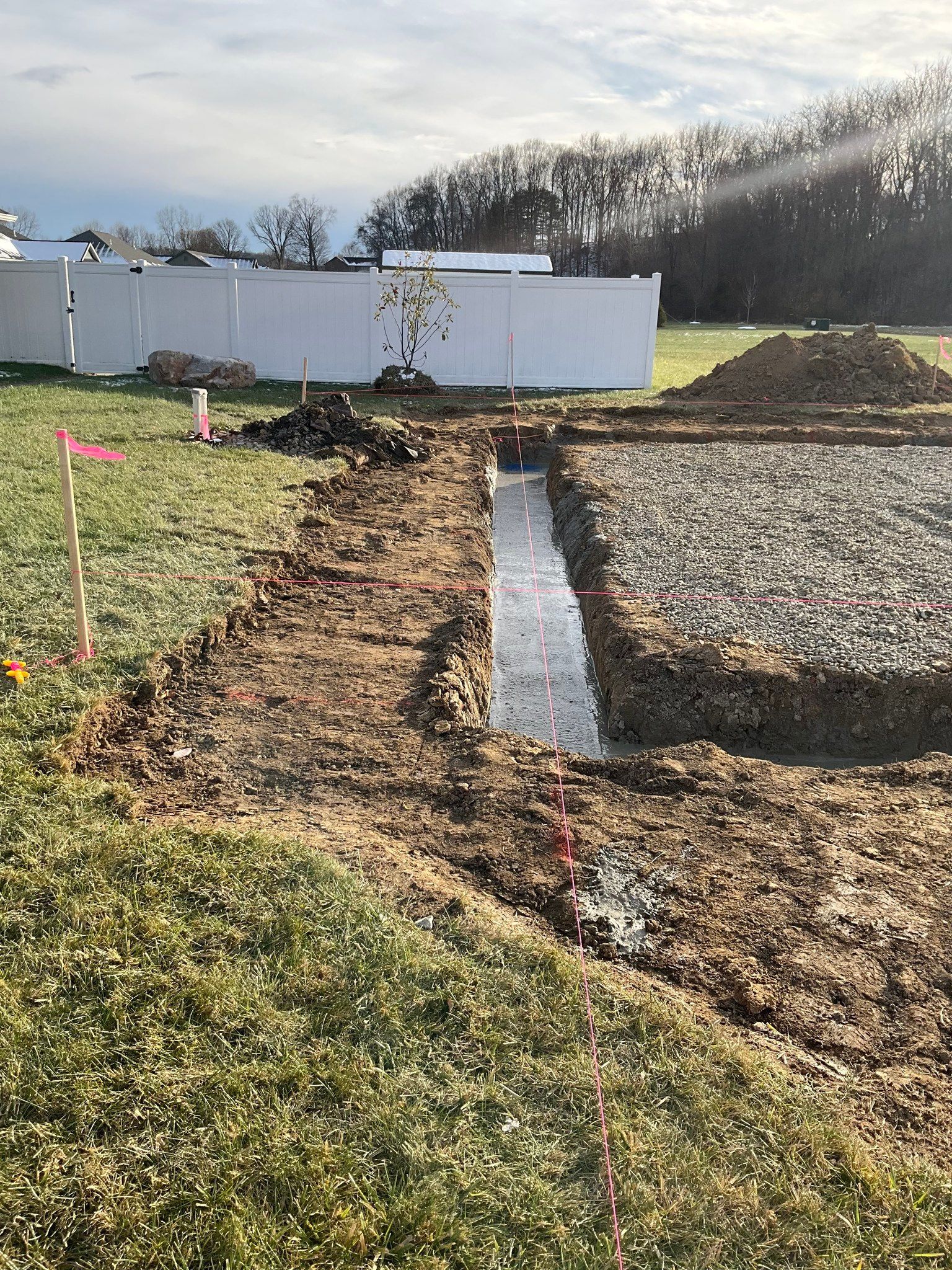 Construction site with a narrow concrete trench, dirt piles, and a white fence under a clear sky