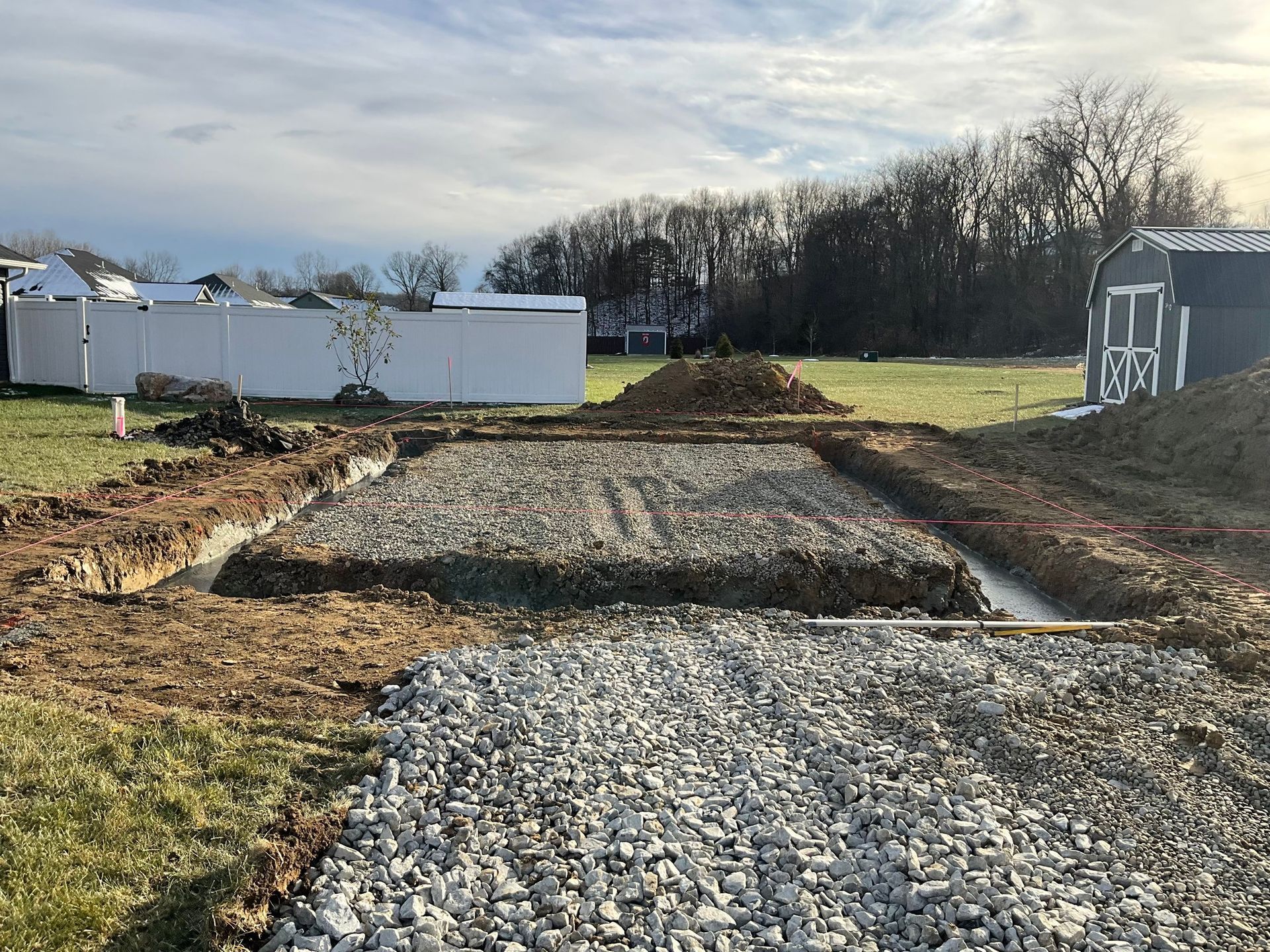 Gravel driveway under construction in a rural yard, with dirt piles and a white shed in the background