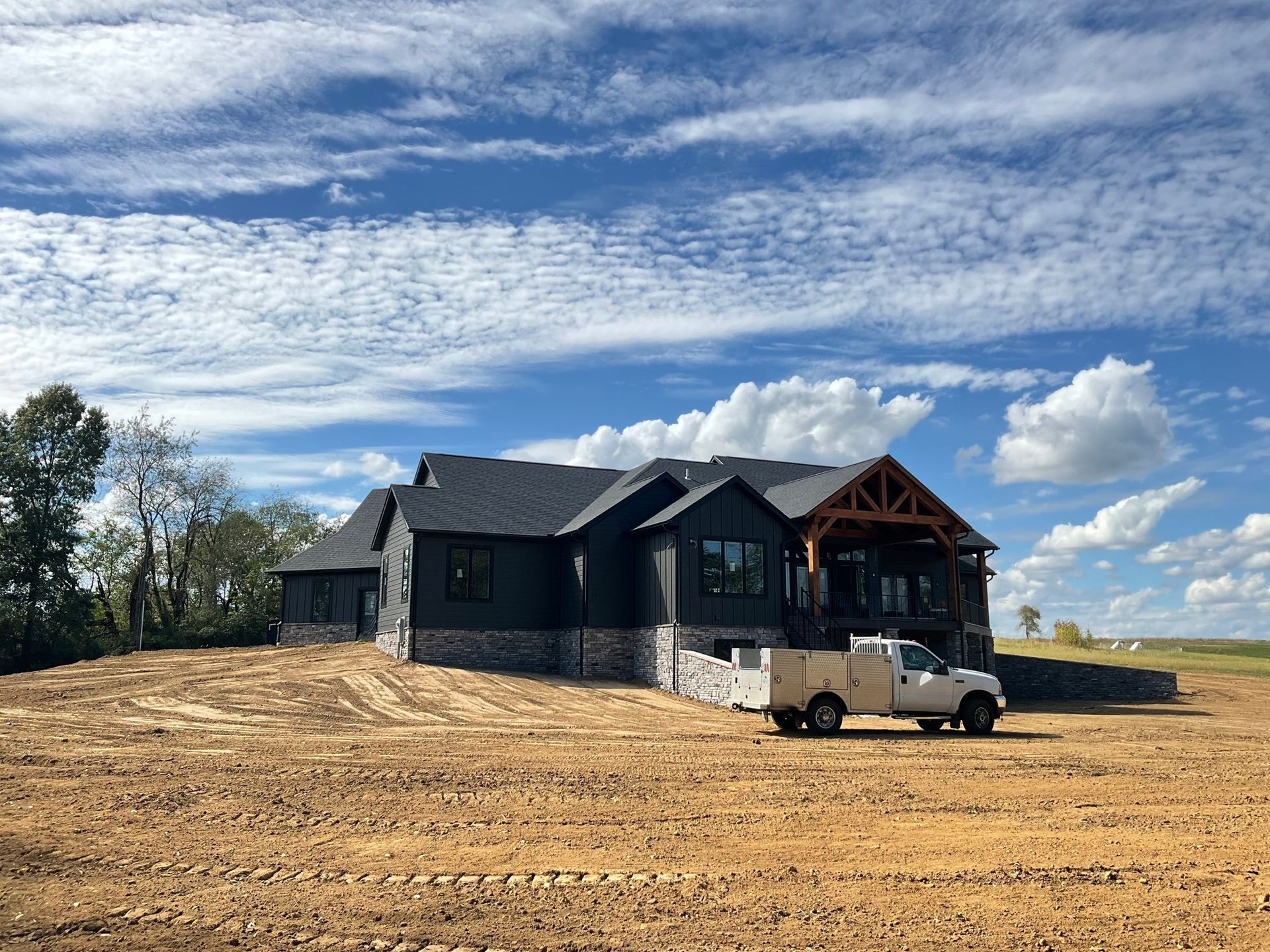 Stone house under construction on a bare lot, with a pickup truck and cloudy sky.