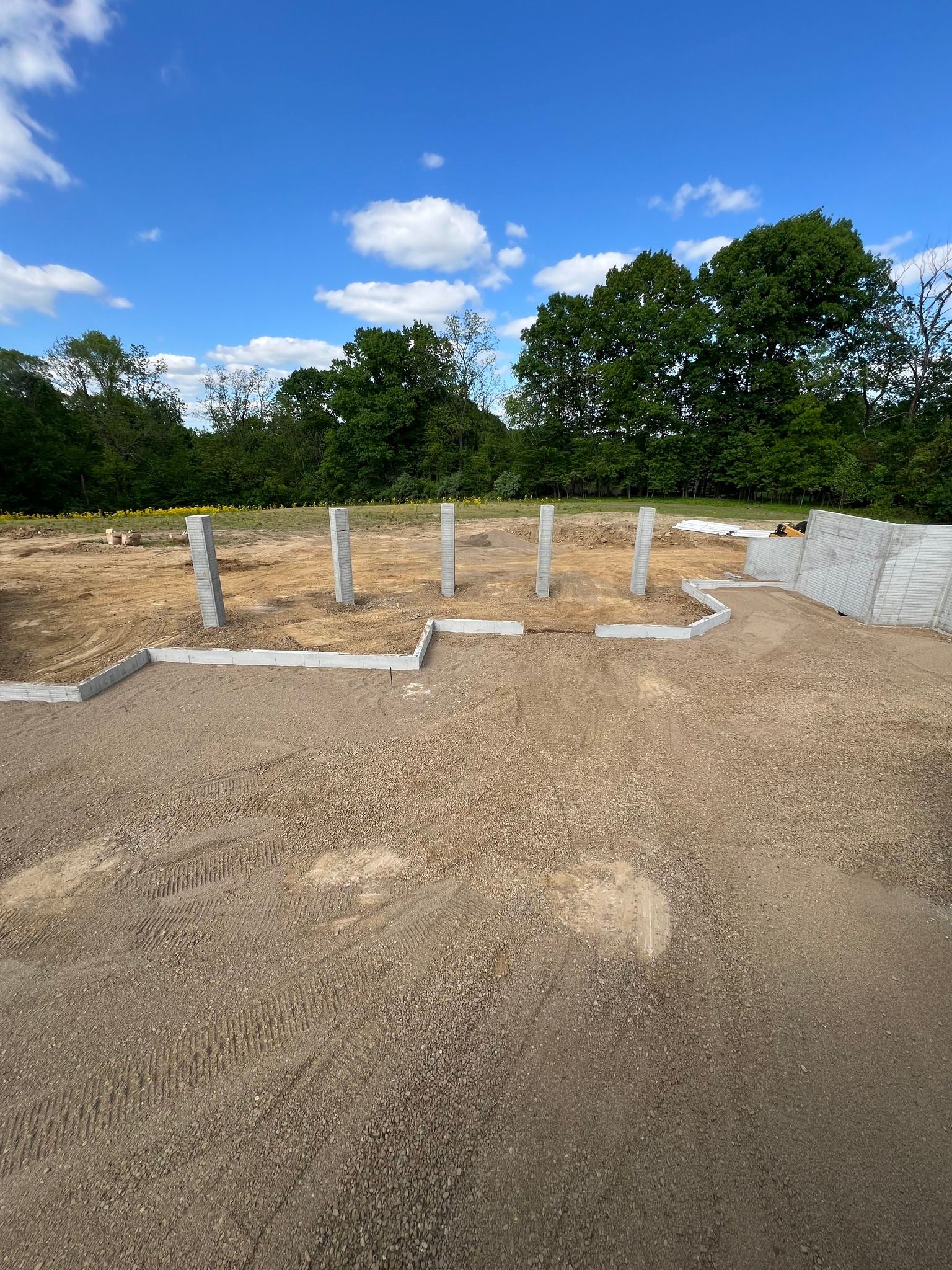 Gravel construction site with concrete posts, white edging, and trees under a blue sky