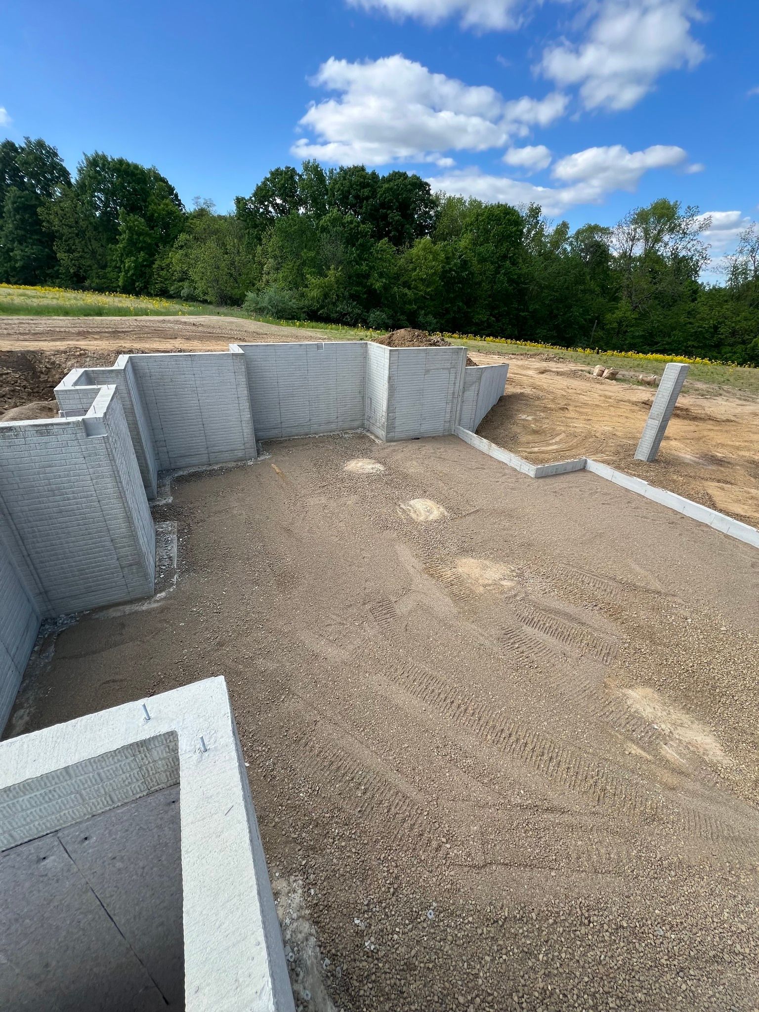 Concrete foundation walls under construction on a gravel site with trees and blue sky in the background