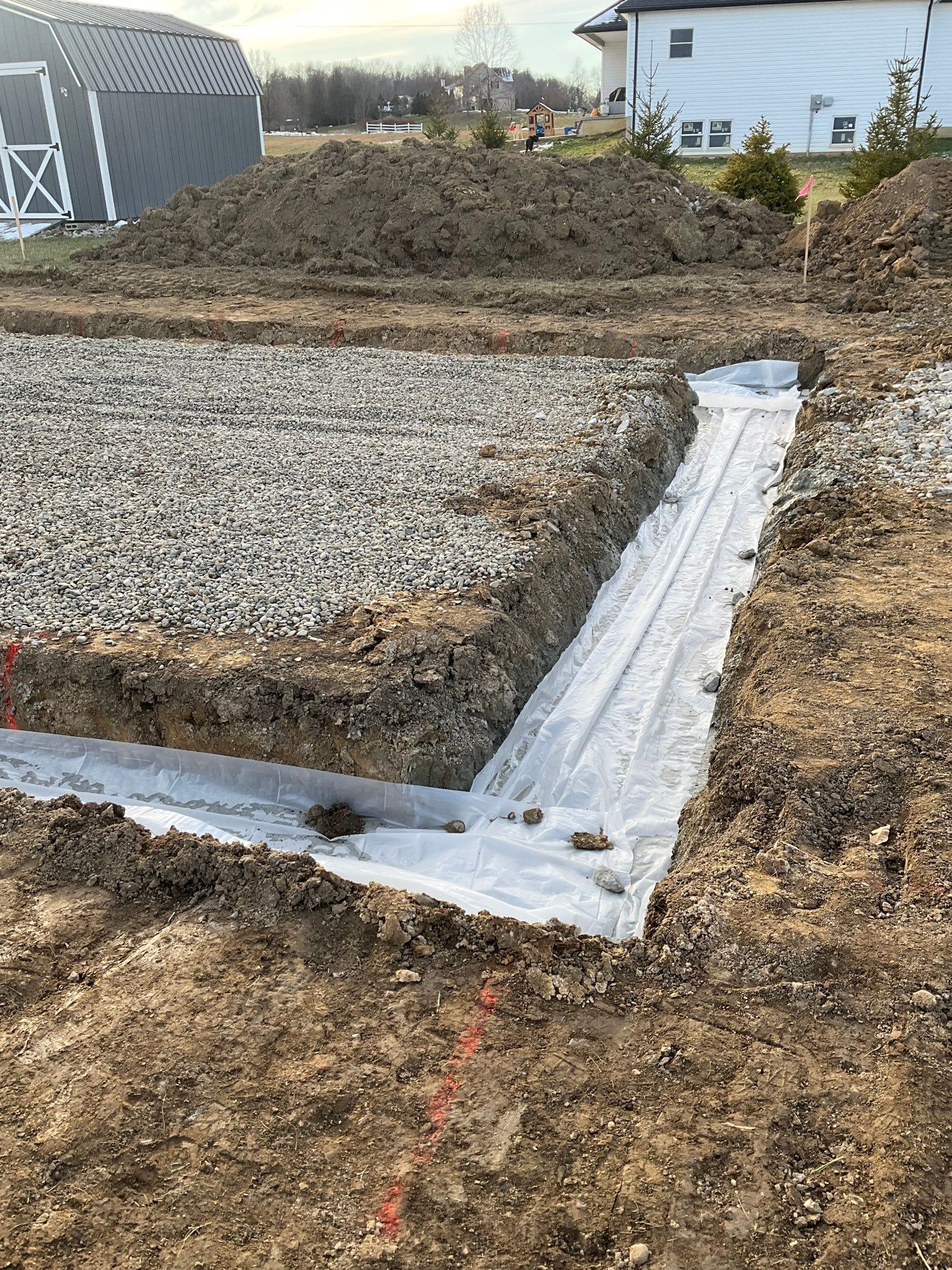 Gravel foundation with white drainage trench and mounded soil at a construction site