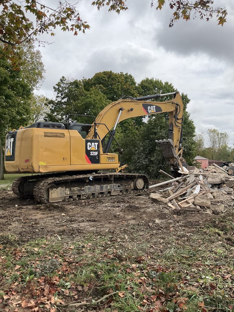 Yellow excavator clearing rubble at a demolition site under cloudy skies