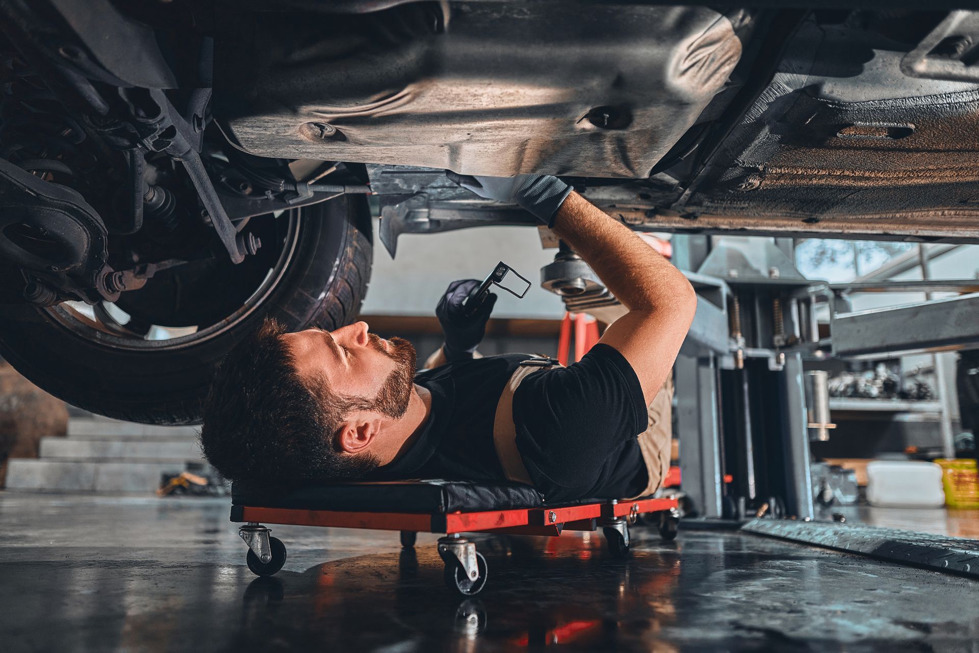 A mechanic is lying under a vehicle on a creeper, inspecting with a flashlight. A mechanic is lying under a vehicle on a creeper, inspecting with a flashlight.