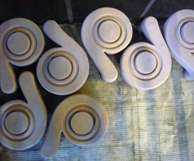 Diversi elementi in cemento stampato, di colore chiaro e a forma di spirale, disposti su una superficie di lavoro.