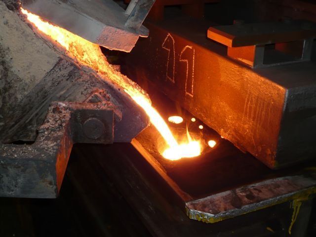 Metallo fuso che viene versato da uno scivolo in uno stampo contrassegnato dal numero 11 in un contesto industriale.