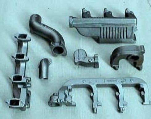 Una varietà di collettori e tubi metallici industriali per motori automobilistici disposti su uno sfondo chiaro.