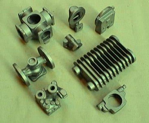 Un assortimento di vari componenti industriali in metallo fuso di colore grigio metallizzato, disposti su uno sfondo chiaro.