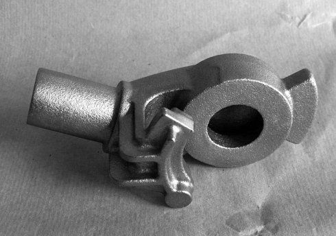 Componente metallico industriale in fusione caratterizzato da un alloggiamento cilindrico, un foro circolare centrale e un braccio sporgente.
