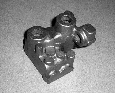 Un componente meccanico in metallo grigio con molteplici fori e sporgenze cilindriche, probabilmente un componente fuso di un motore o di una macchina.