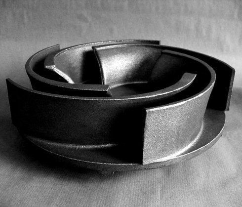 Girante di una pompa centrifuga scura e metallica con pale curve, su uno sfondo neutro e ombreggiato.