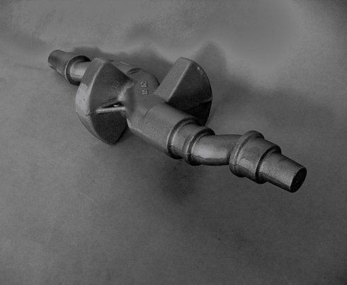 Un albero motore metallico scuro con contrappeso centrale, posizionato diagonalmente su uno sfondo neutro.