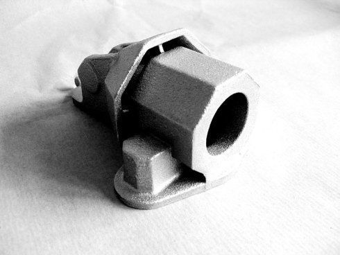 Componente industriale in metallo pressofuso di colore grigio, con sezione cilindrica esagonale e base di montaggio piatta.