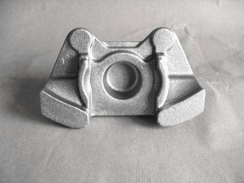 Un componente metallico industriale in fusione con una depressione circolare centrale e flange laterali simmetriche su sfondo grigio.