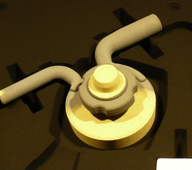 Un prototipo industriale di colore grigio e beige, dotato di due bracci tubolari, è riposto in una custodia nera foderata di schiuma.