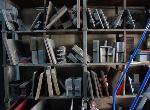Componenti e lamiere metalliche industriali stoccate in una scaffalatura di legno a più livelli.
