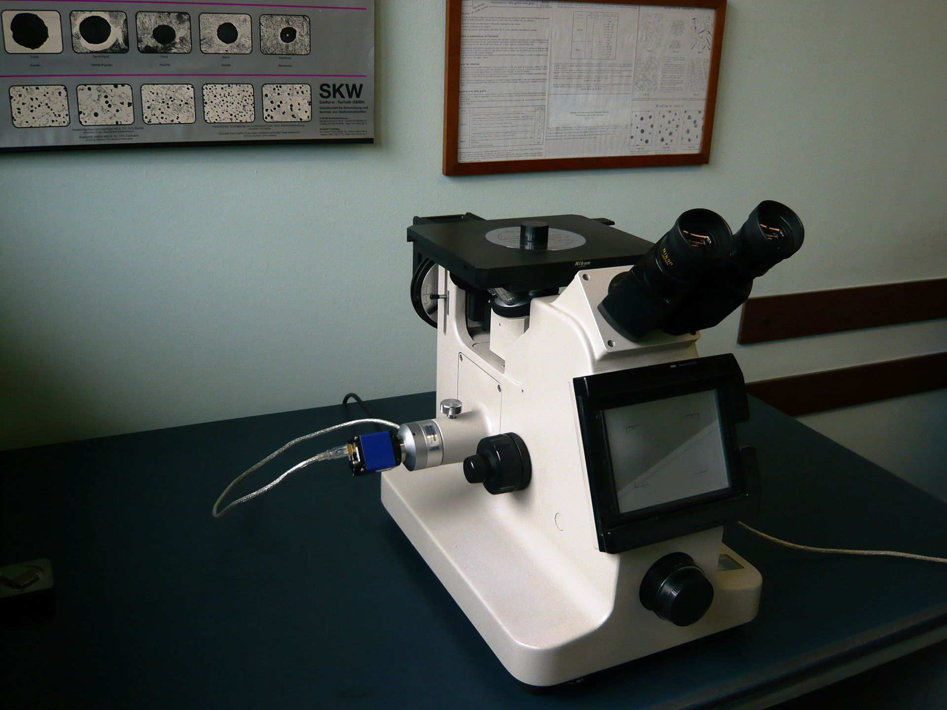 Un microscopio medico con schermo digitale integrato, posizionato su un tavolo in un ambiente clinico o di laboratorio.