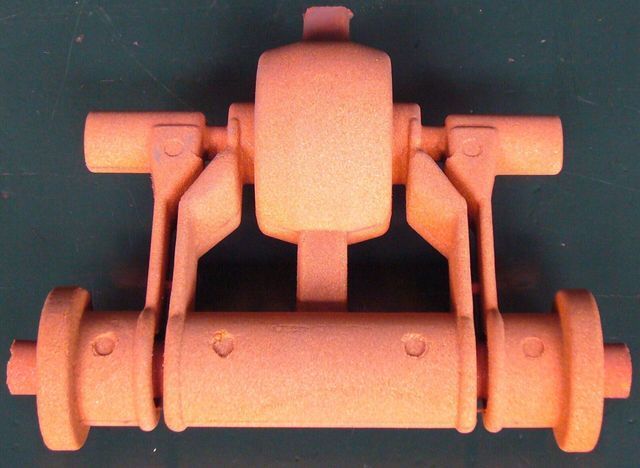 Un gruppo meccanico arancione stampato in 3D, composto da un alloggiamento centrale, due bracci pivotanti e un componente a rullo inferiore.