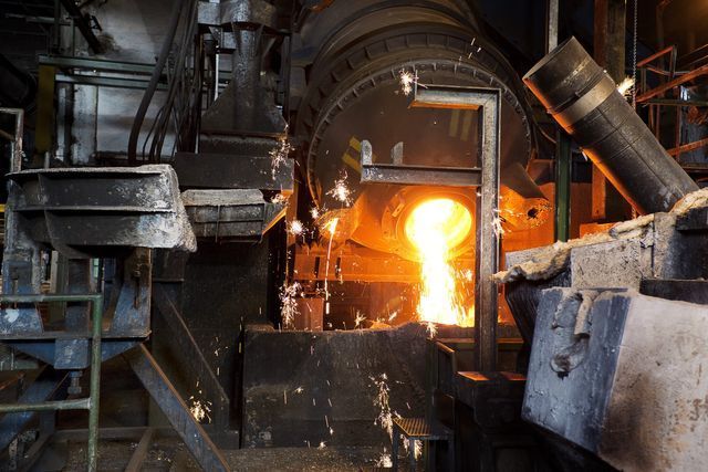 In uno stabilimento di produzione, il metallo fuso fuoriesce da un forno industriale incandescente e si riversa in una vasca di raccolta.