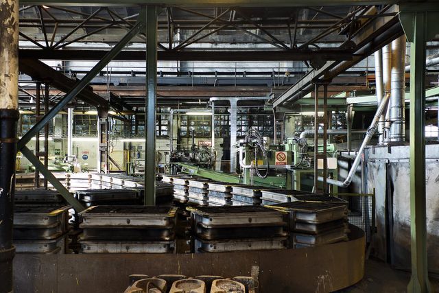 Nell'area di uno stabilimento industriale è presente un grande sistema di nastri trasportatori circolari e scuri che spostano stampi metallici attraverso una zona meccanica.