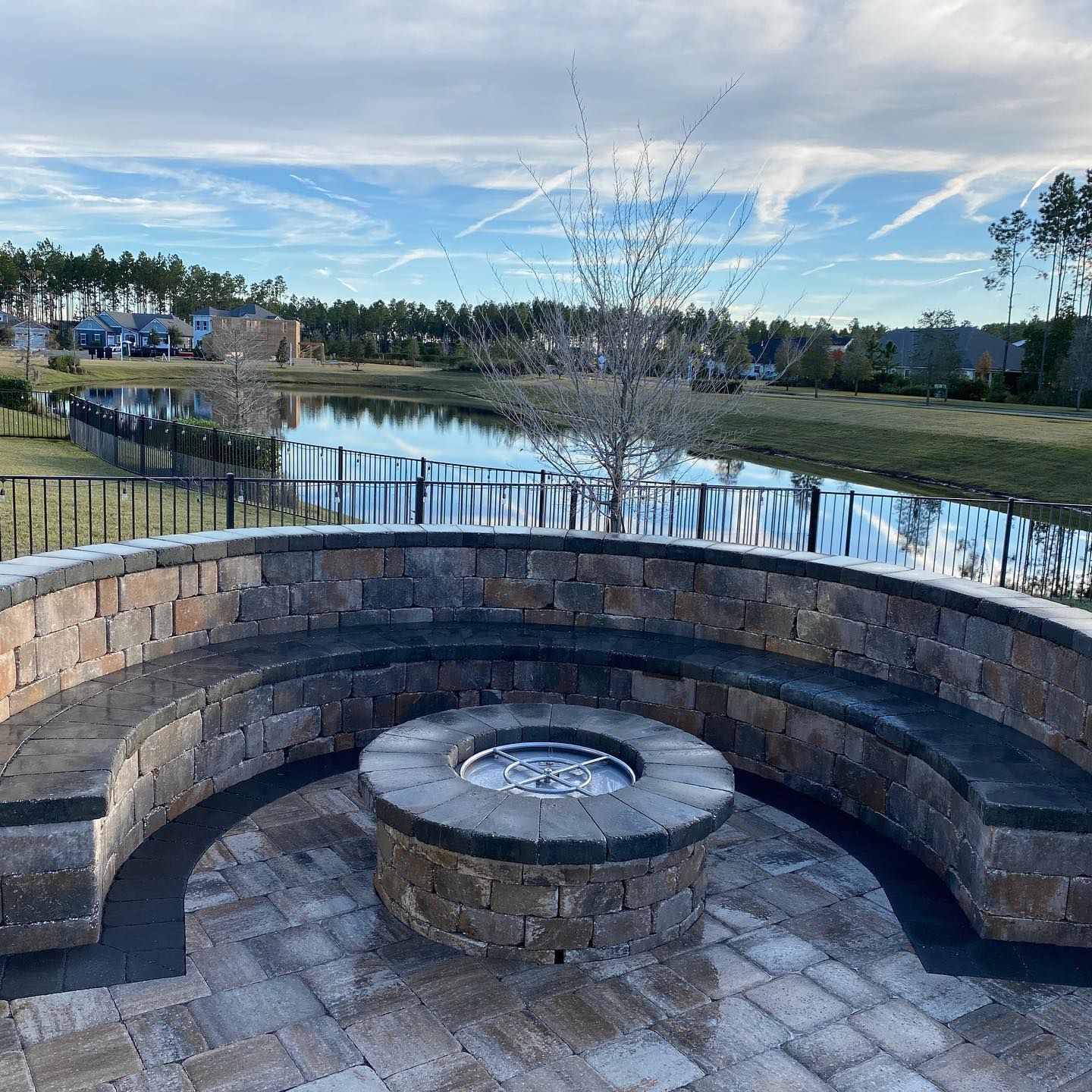A fire pit with a bench around it and a lake in the background