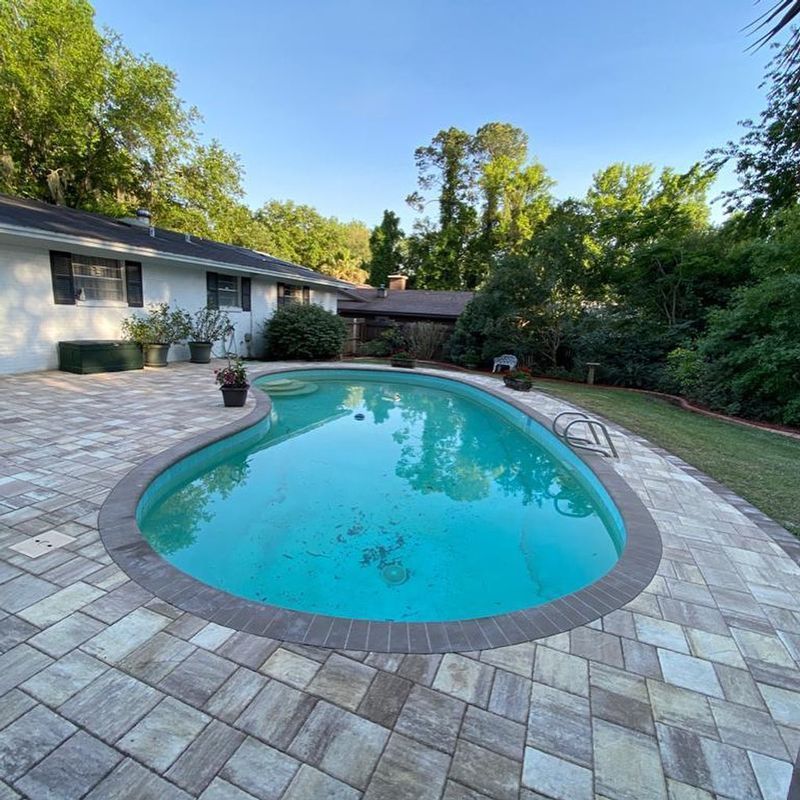 A large swimming pool in the backyard of a house with brick pavement.