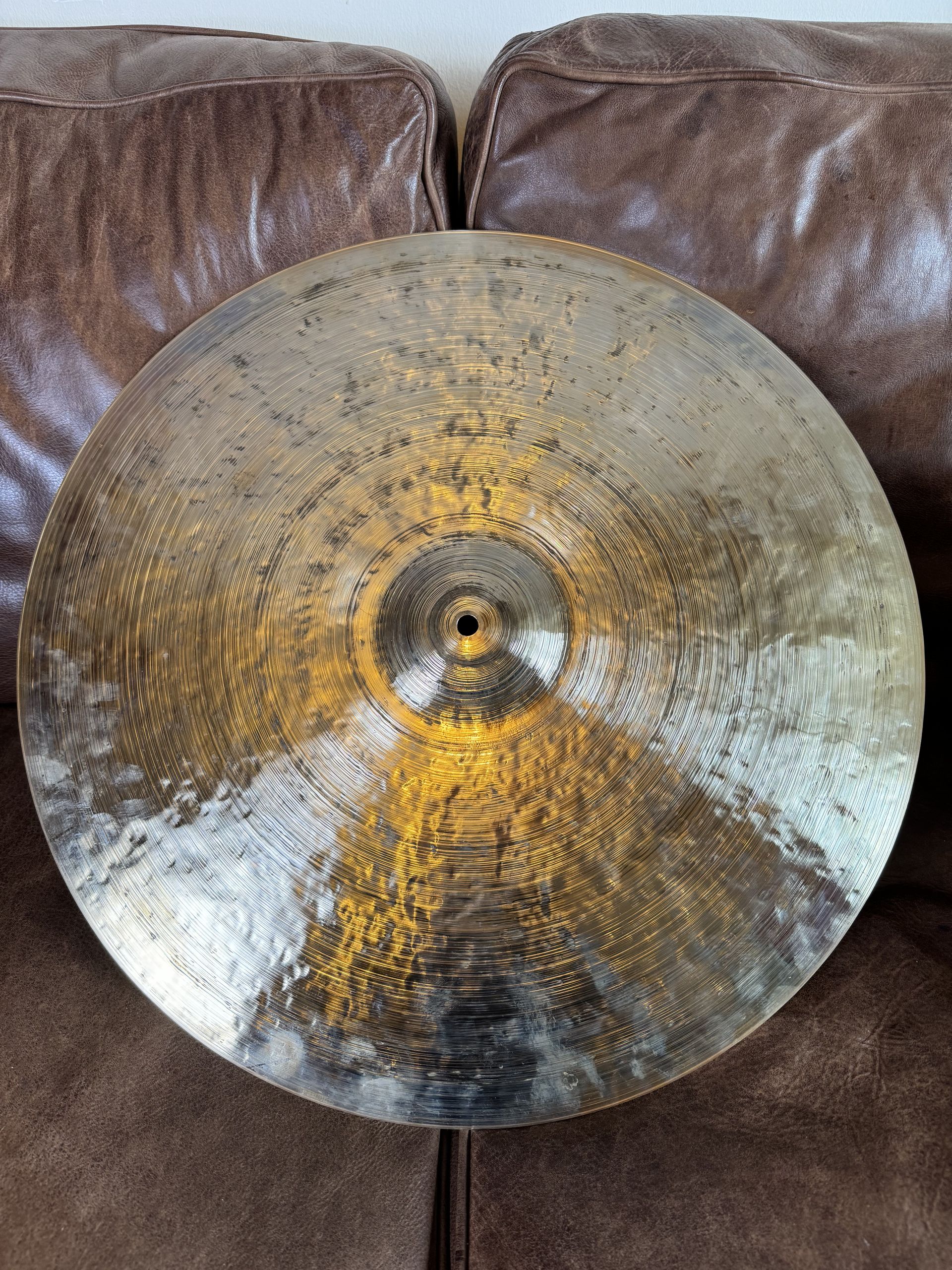 Bronze cymbal, circular with a central hole, resting on a brown leather couch.
