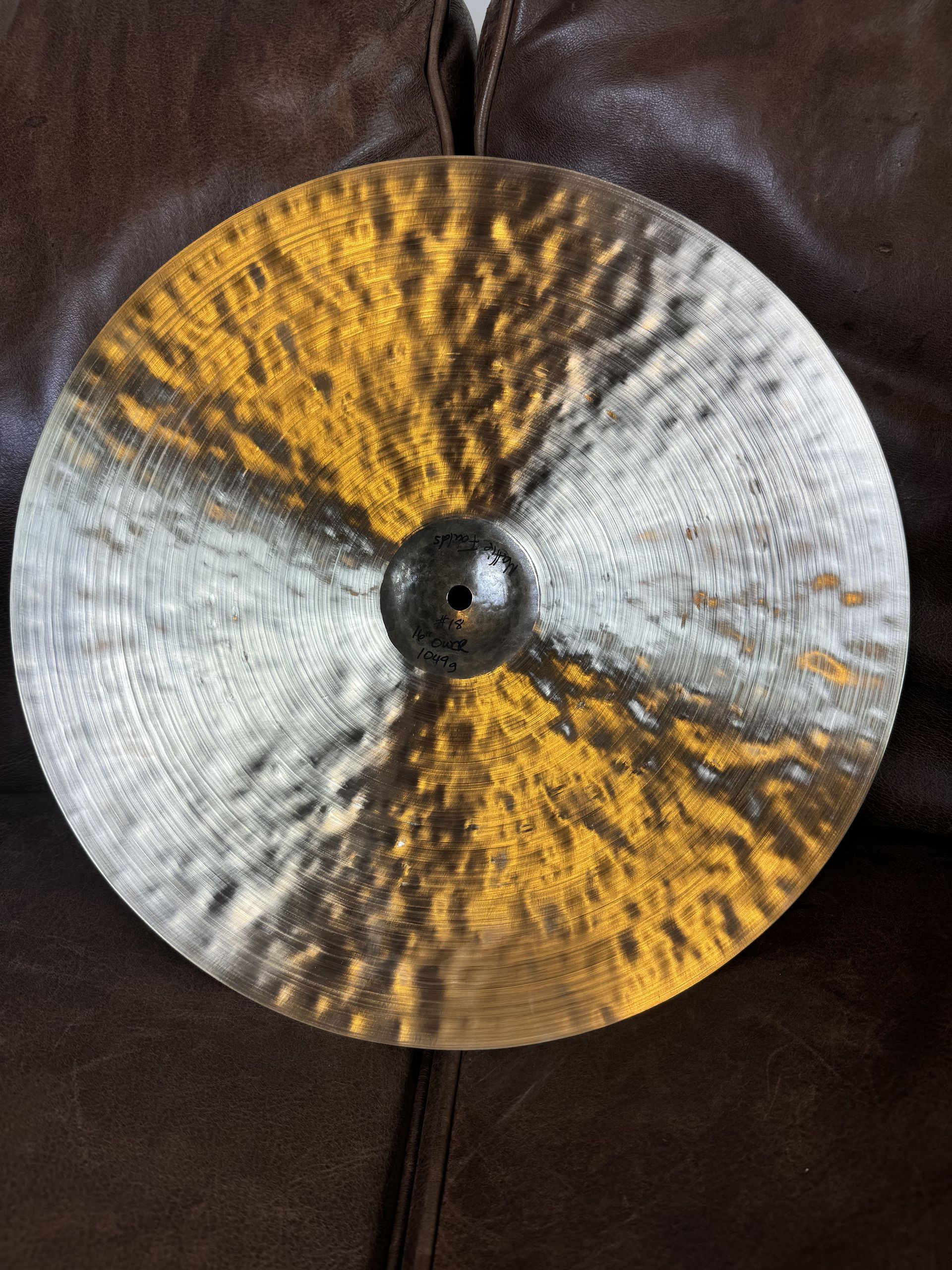 Dark cymbal with gold and silver hues on a brown leather surface.