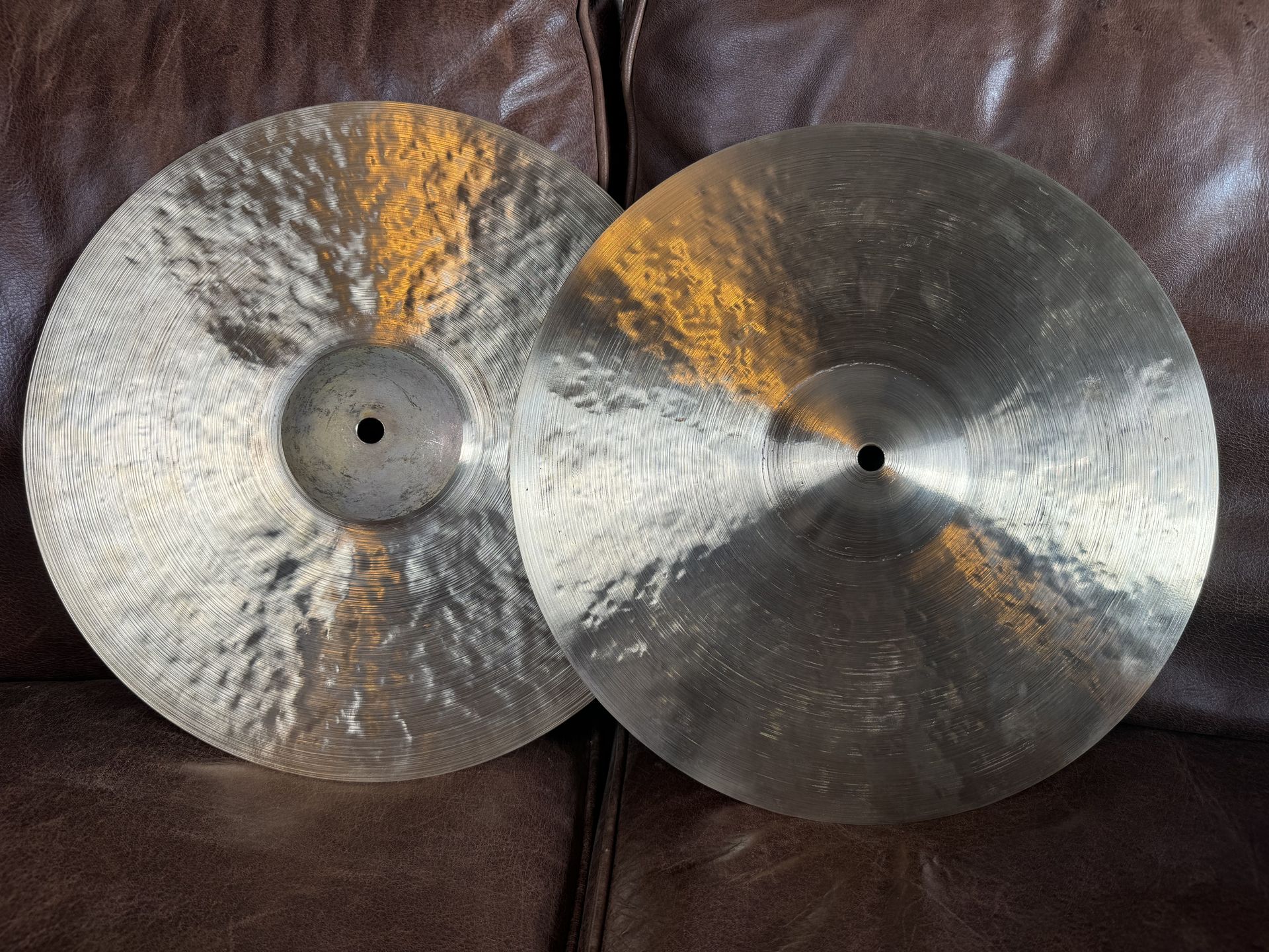 Two cymbals, possibly for a drum set, on a brown surface, with a metallic sheen and central holes.
