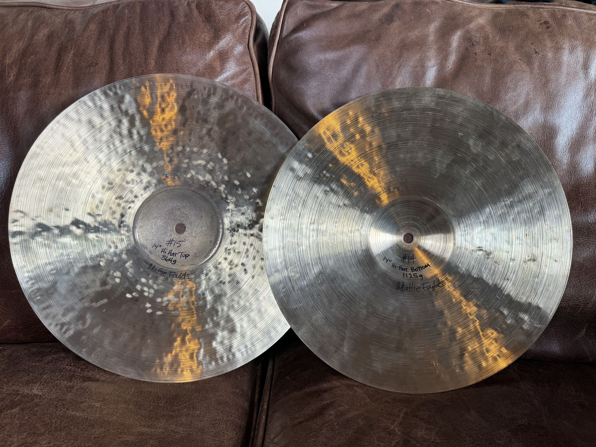 Two cymbals, possibly for a drum set, on a brown surface, with a metallic sheen and central holes.