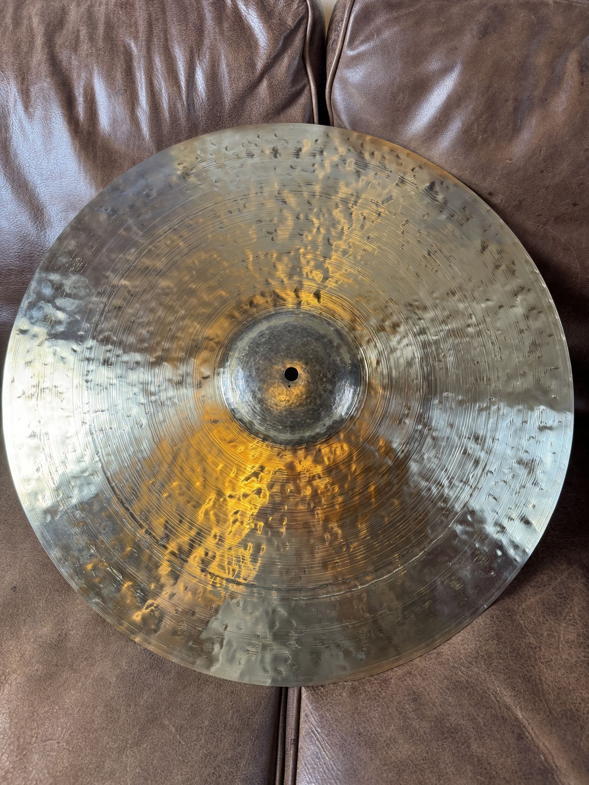 Bronze cymbal with a square hole, resting on a brown leather surface.