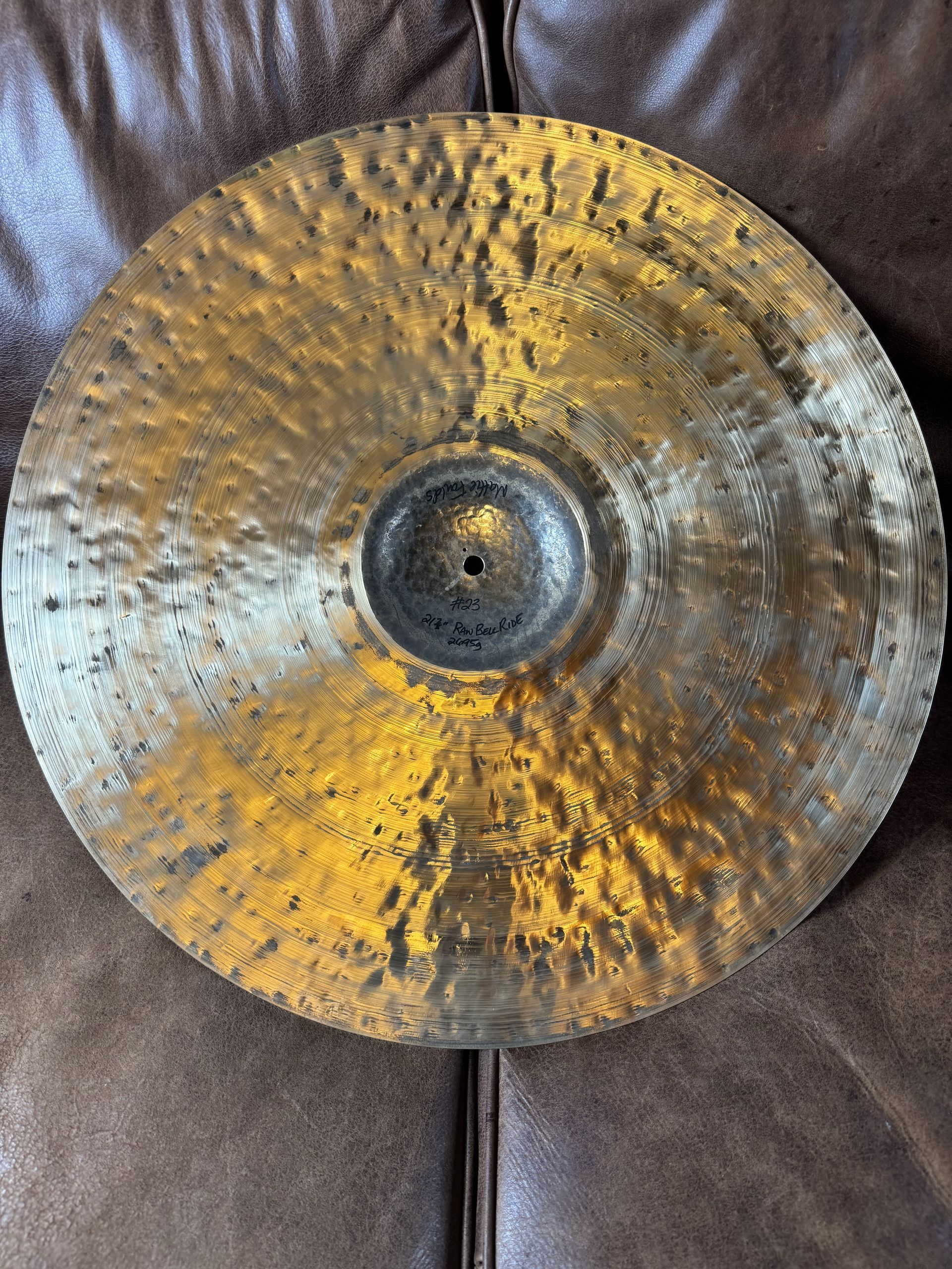 Bronze cymbal with a square hole, resting on a brown leather surface.