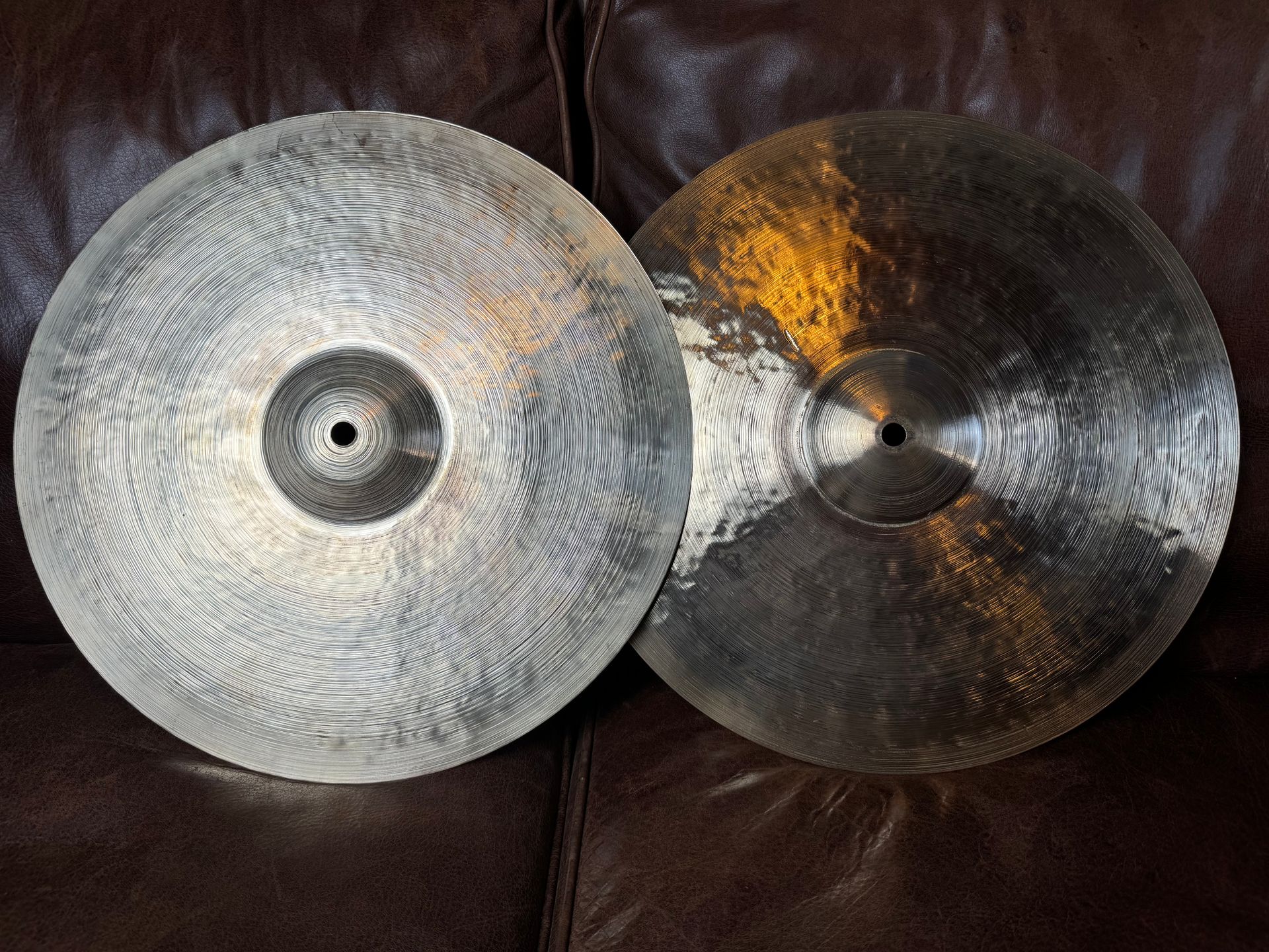 Two cymbals, one silver-toned and one gold-toned, resting on a brown leather surface.