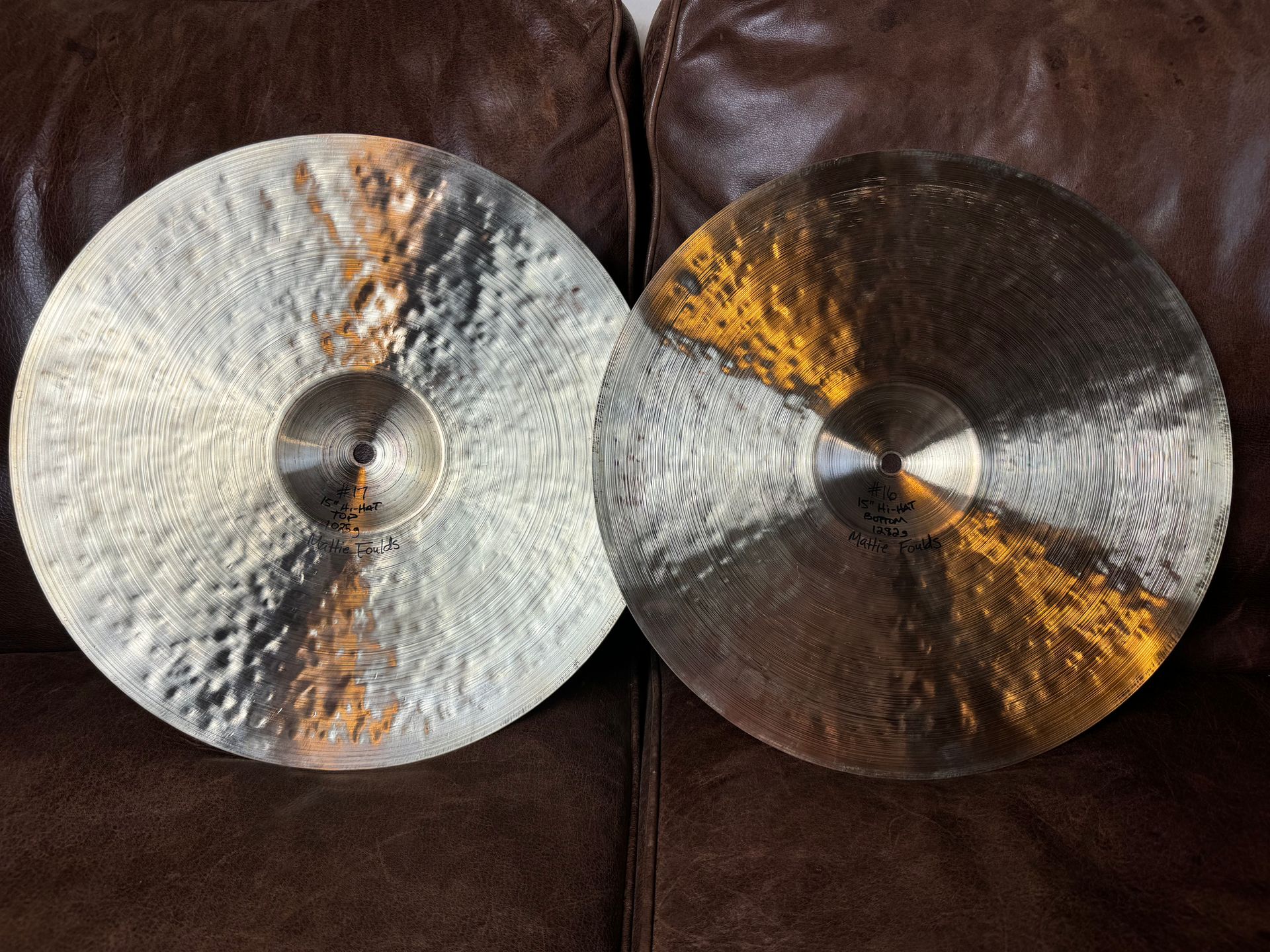 Two cymbals, one silver-toned and one gold-toned, resting on a brown leather surface.