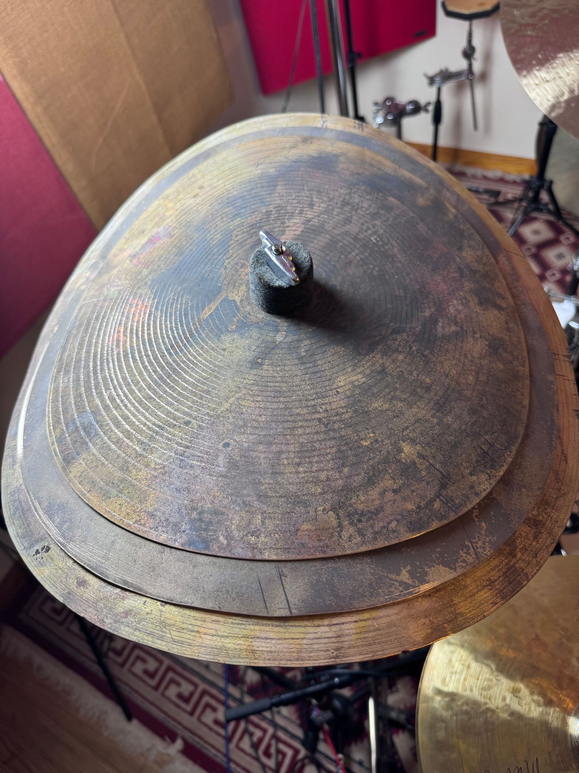 A rusty, layered cymbal with a black top piece sits atop a drum set.