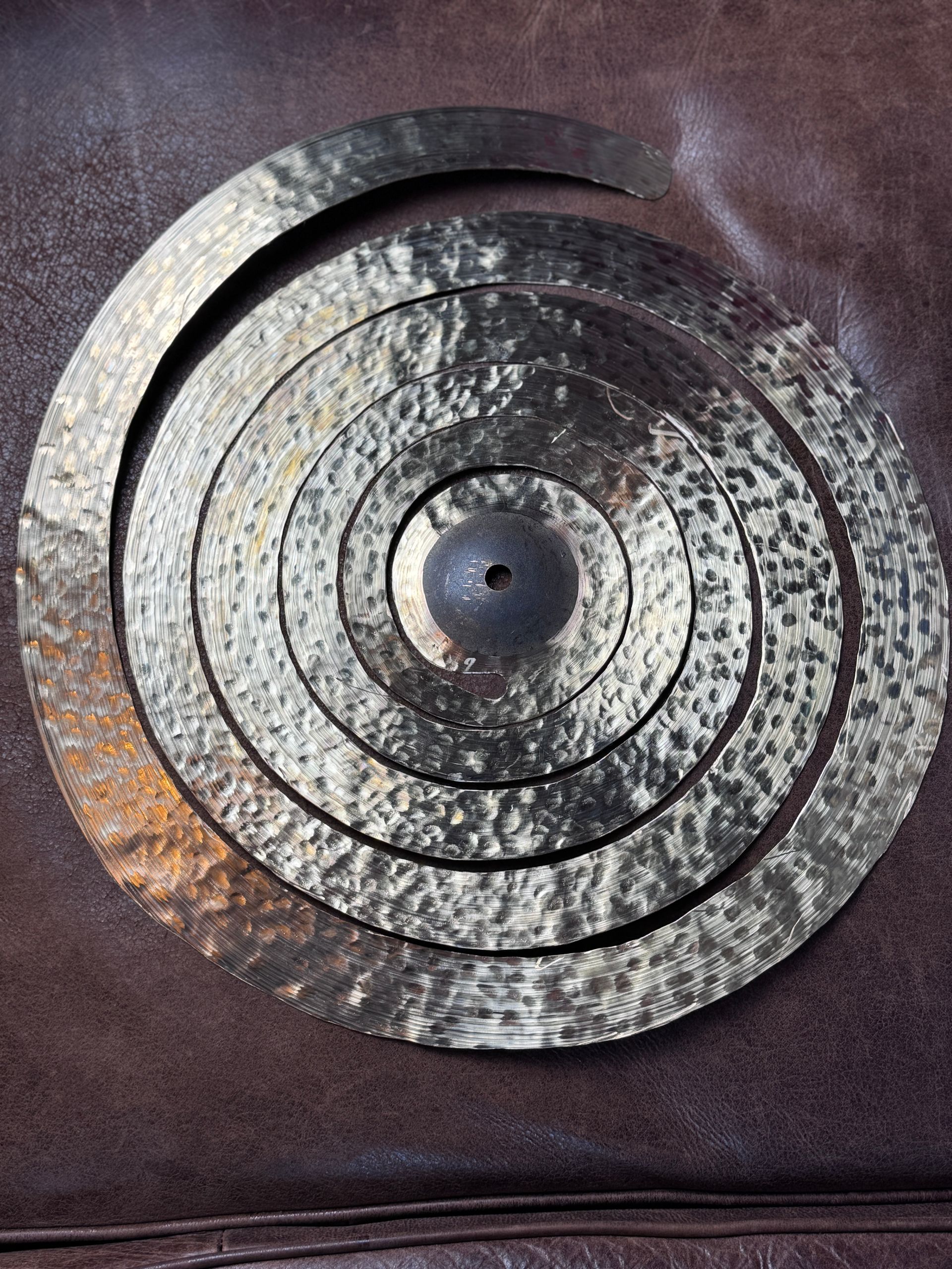 A spiral-shaped cymbal, dark bronze-colored, with concentric circles, on a brown surface.
