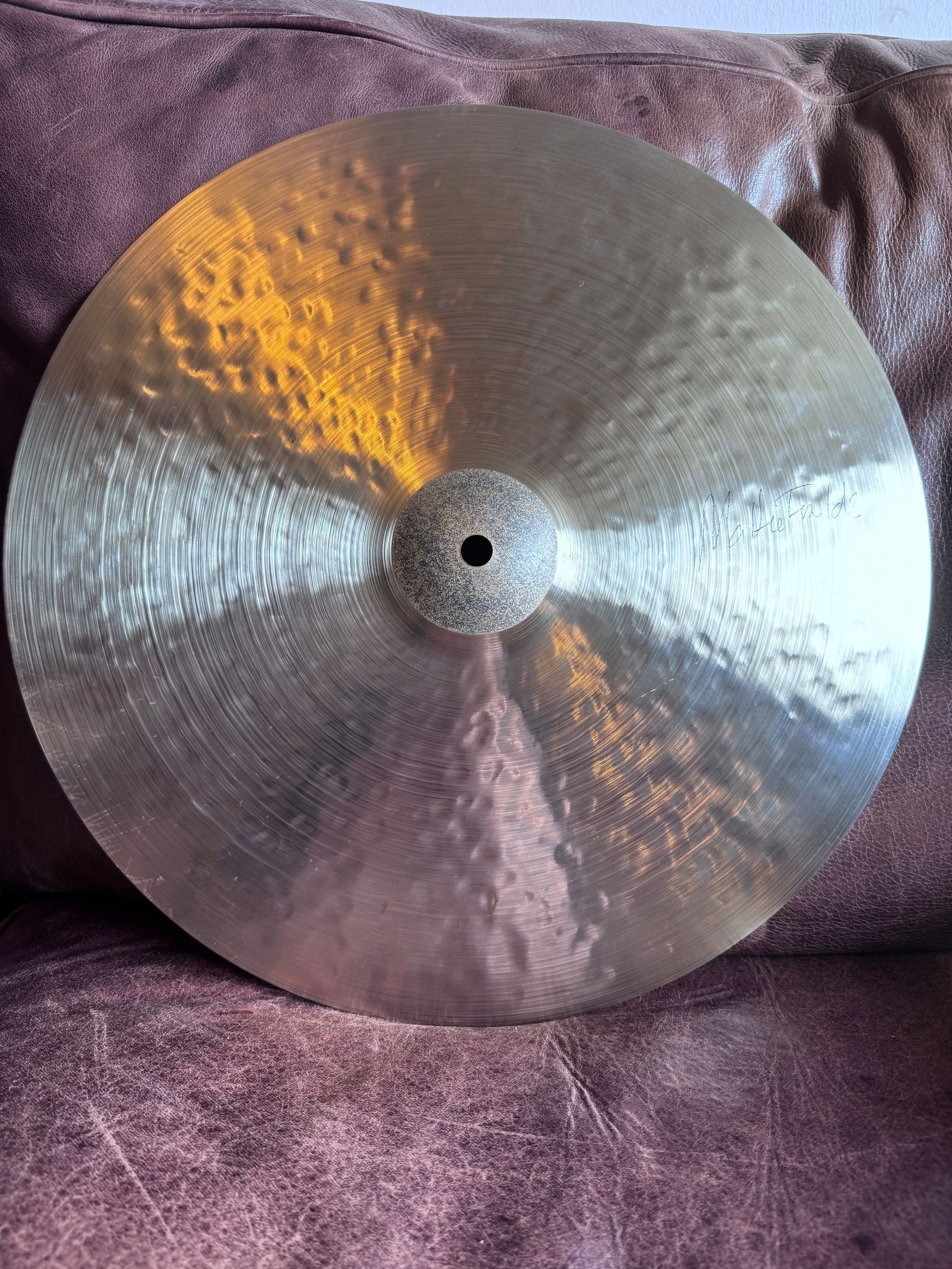 Close-up of a golden cymbal with concentric hammer marks and a small, square hole in the center.