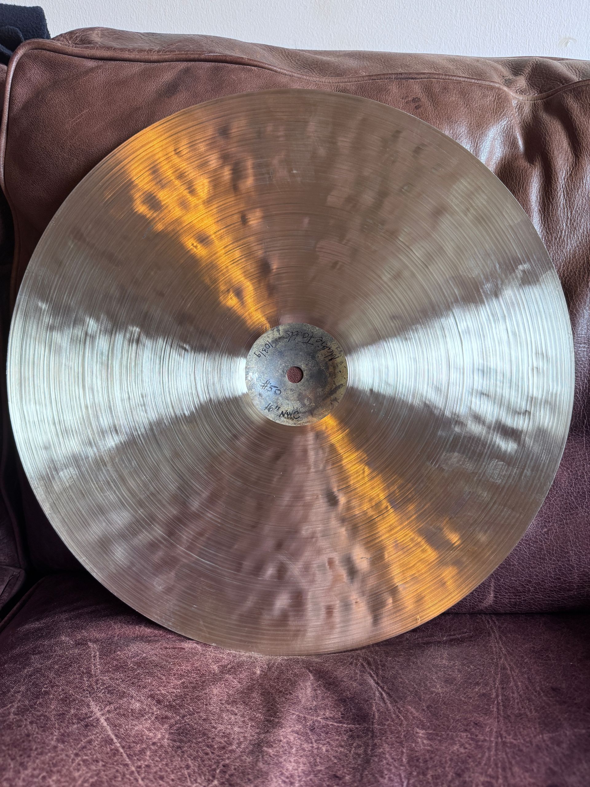 Close-up of a golden cymbal with concentric hammer marks and a small, square hole in the center.