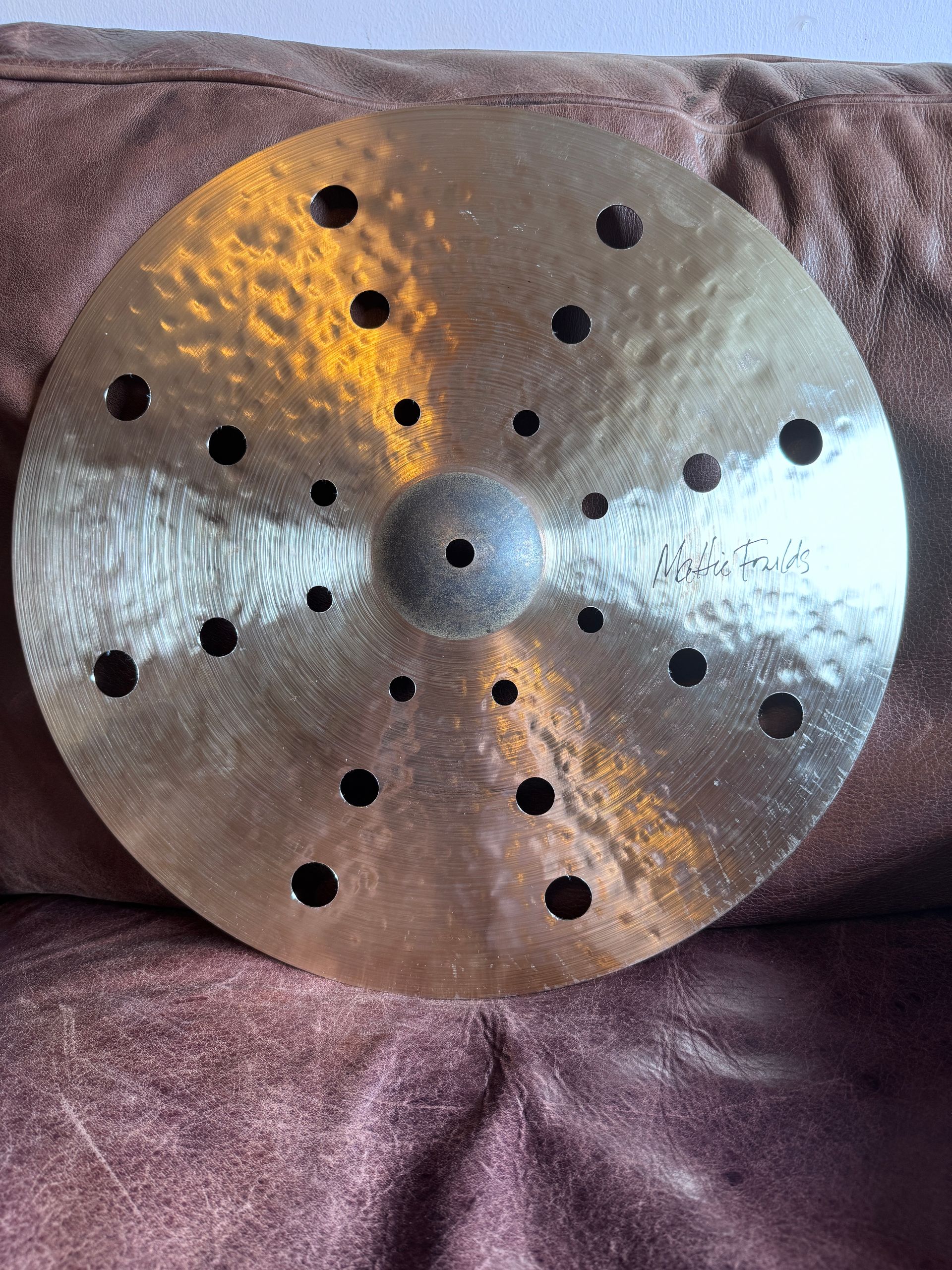 Gold-colored cymbal with holes, resting on a brown surface.